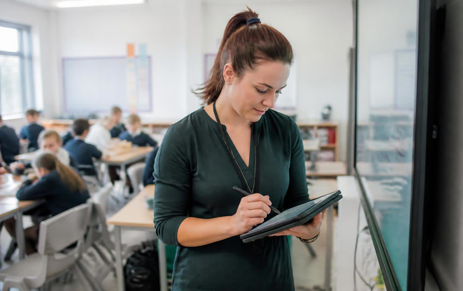 Teacher marking work on a tablet beside an interactive display